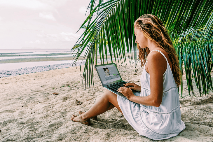 woman on beach searching for online teaching jobs on laptop