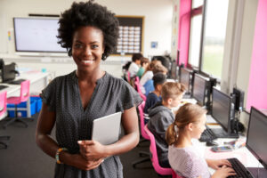woman stands in front of a classroom with kids learning on computers