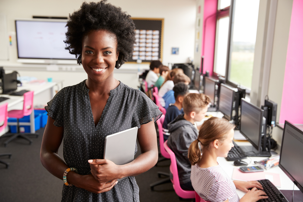 woman stands in front of a classroom with kids learning on computers