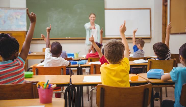 female teacher in class with kids raising their hands - - teaching after college. 