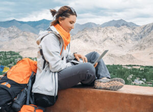 backpacker on laptop studying TEFL certification online while traveling with mountains in background
