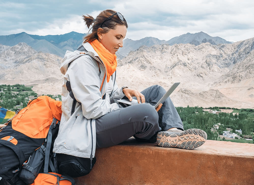 backpacker on laptop studying TEFL certification online while traveling with mountains in background
