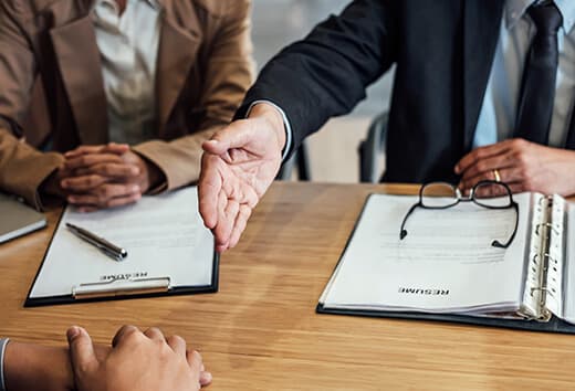 Candidate Sourcing Two recruiters at a table, one stretching out their hand to extend an offer to a candidate - education staffing