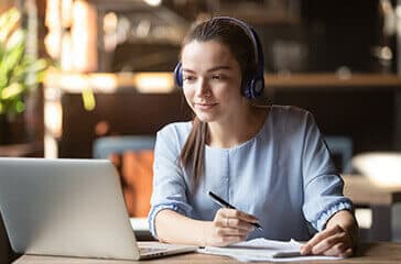 Young woman learning on her laptop, with headphones on - Teacher recruitment online