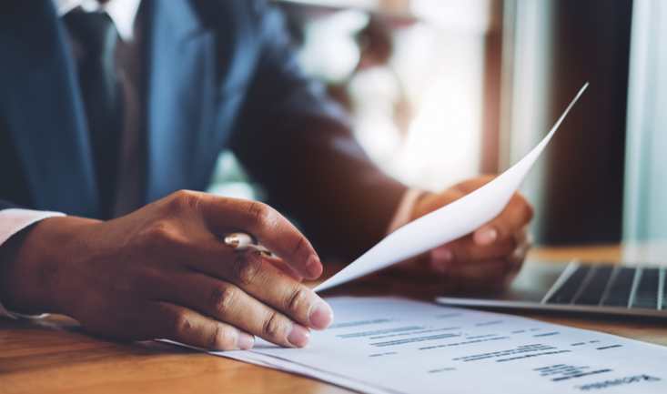 man in suit behind a desk holding a resume