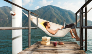 man on a laptop sitting in a hammock by lush green mountains doing an online TEFL program