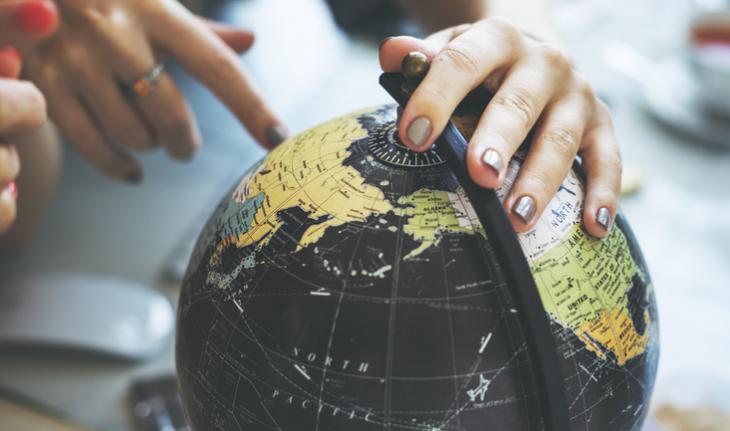 hand on a globe pointing to an unseeable destination