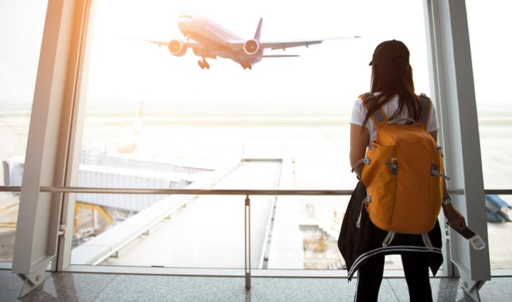 woman in a backpack at the airport watching an airplane