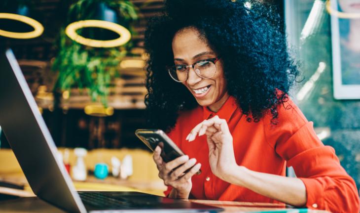 cheerful woman downloading online teaching apps for esl teachers at a laptop and holding a phone