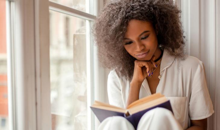 woman sitting by a window happily reading a book