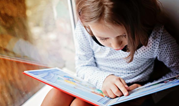 young girl reading a book by the window