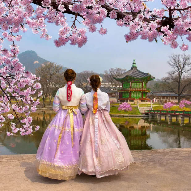 two women in traditional clothing standing in front of a lake and pagoda